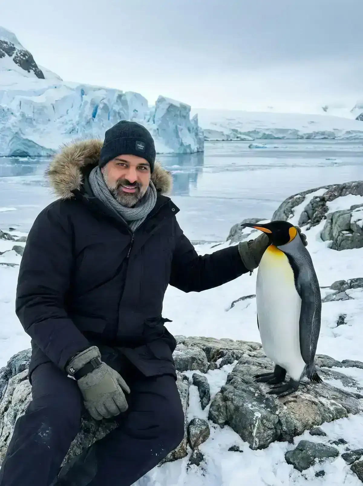 photograph of a young man sitting naturally on a jagged, snowy rock in an icy Antarctic habitat